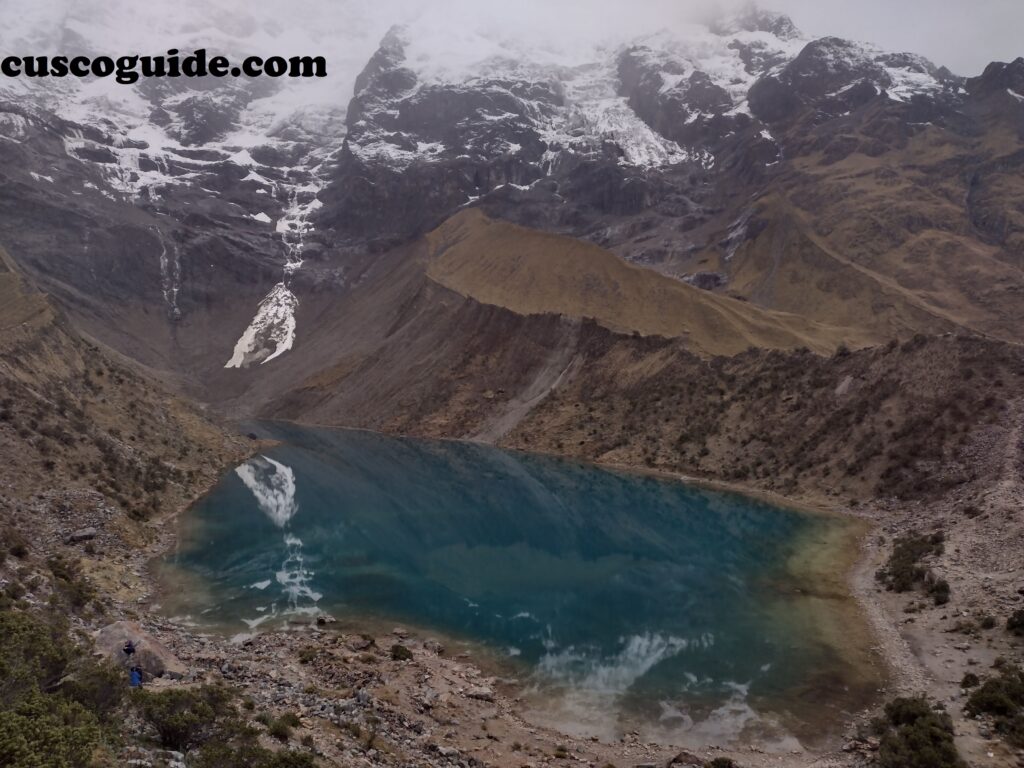 A panoramic view of Humantay Lake, a turquoise glacial lake surrounded by snow-capped peaks in the Peruvian Andes.
