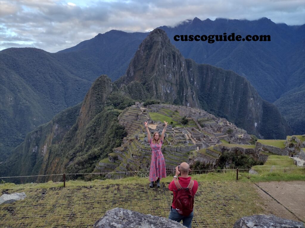 A panoramic view of Machu Picchu from its upper section, showcasing the iconic Inca citadel surrounded by lush green mountains.